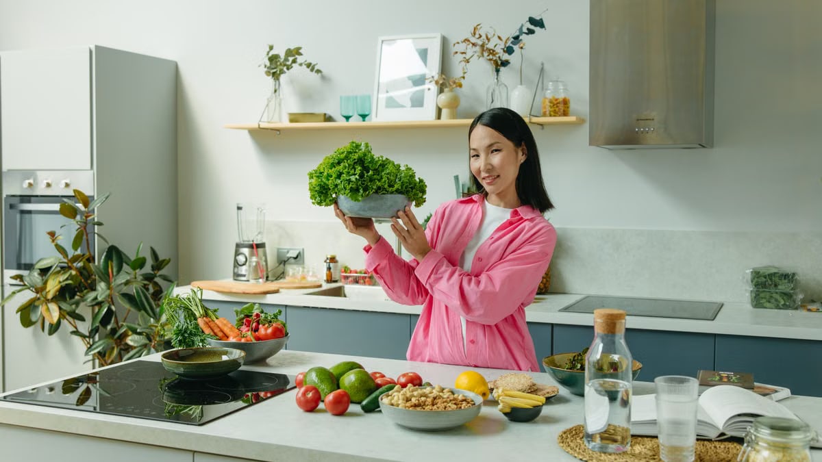 Woman in a kitchen holding fresh lettuce, surrounded by healthy ingredients like tomatoes and avocados, promoting healthy eating.
